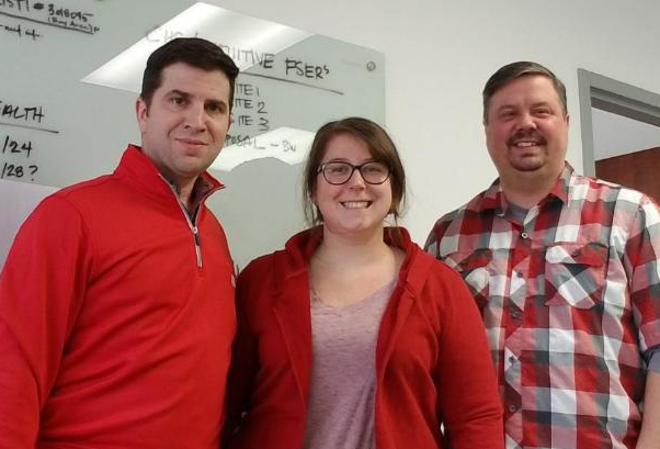 Three people wearing red shirts in front of whiteboard 