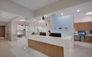 Hospital emergency room station in large, white corridor and blue wall next to patient rooms