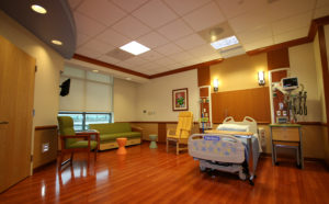 Brightly lit patient room with hospital bed couch and glossy wood floors