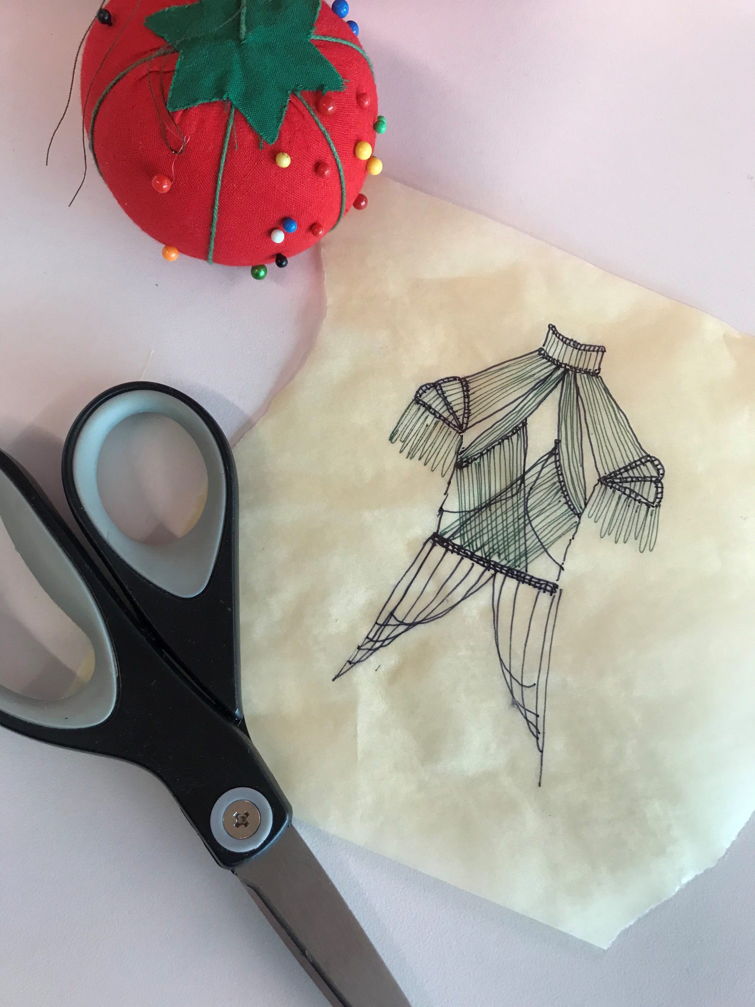 Fashion drawing of shirt next to scissors and red pin cushion