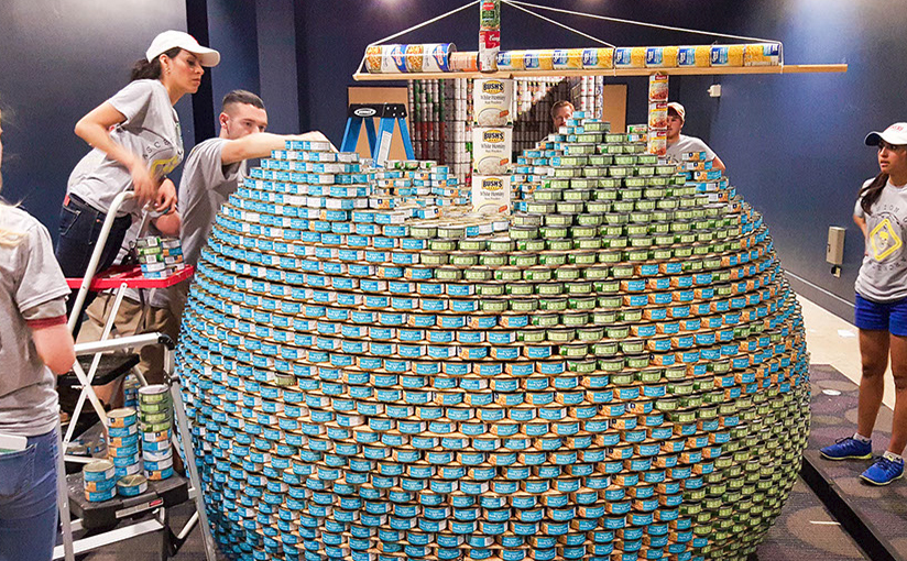 Team of employees working together to build a large globe out of different colored cans