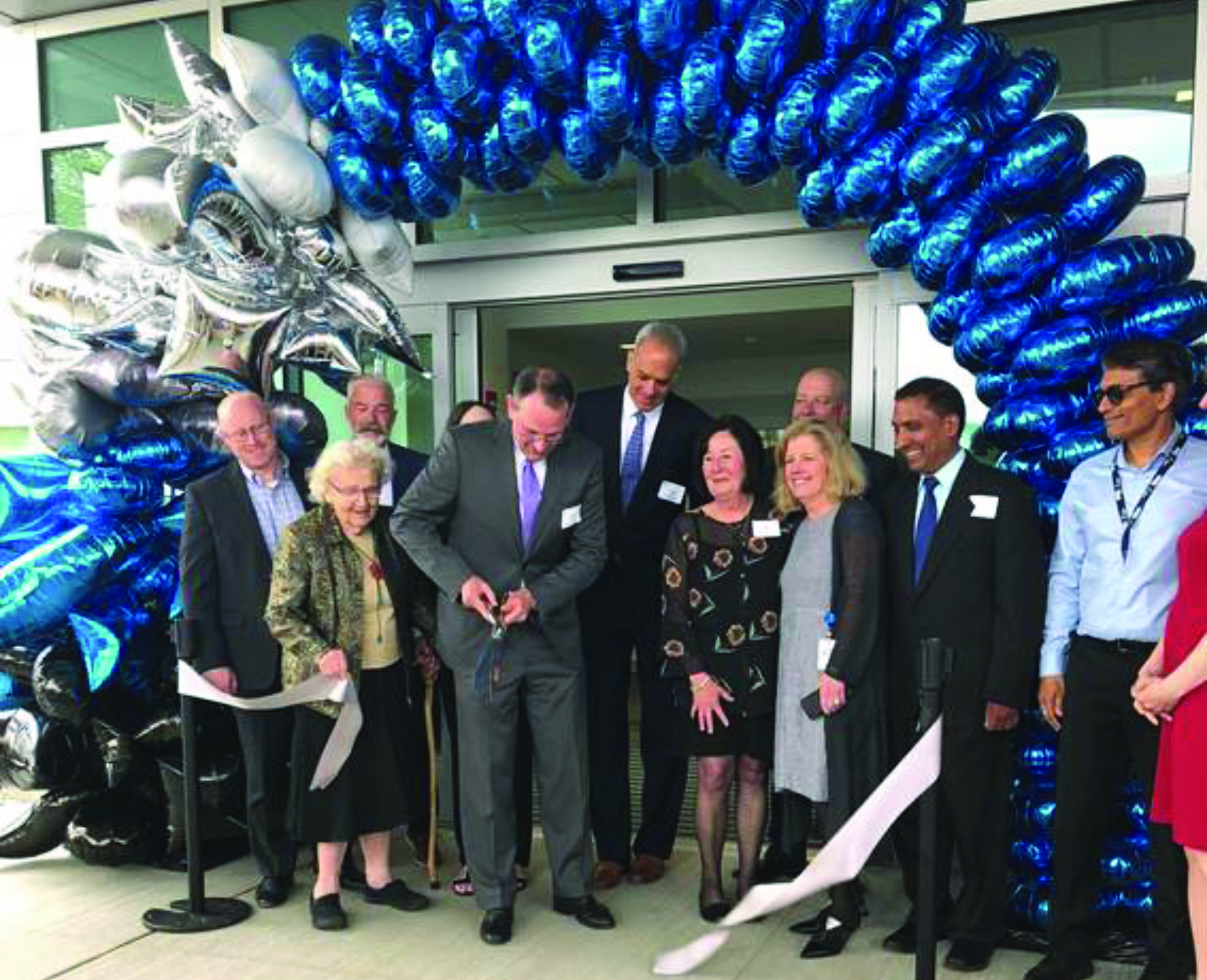 Group of people in business suits with arch of blue balloons cut ribbon at entrance of the Wentworth-Douglas Cancer Center