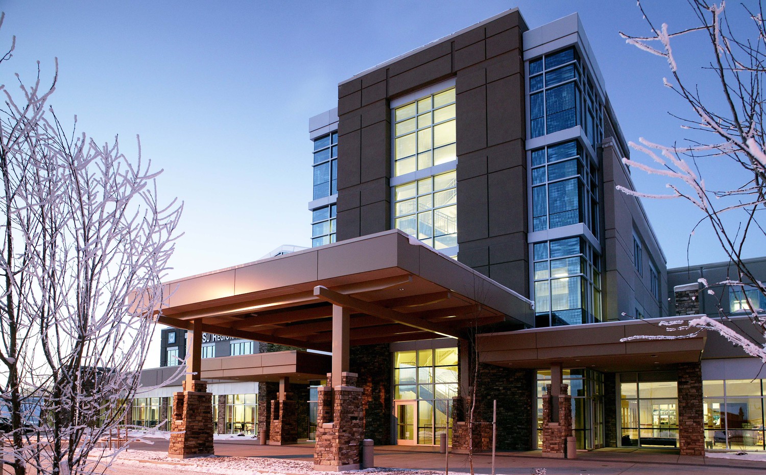 Mat-Su Regional Medical Center entryway with large glass windows, brick accents, and snow-covered trees