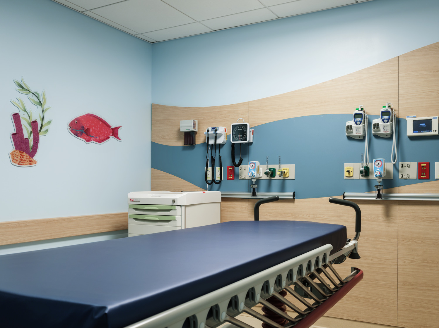 Pediatric exam room with table, storage areas, equipment and under the sea wall graphics