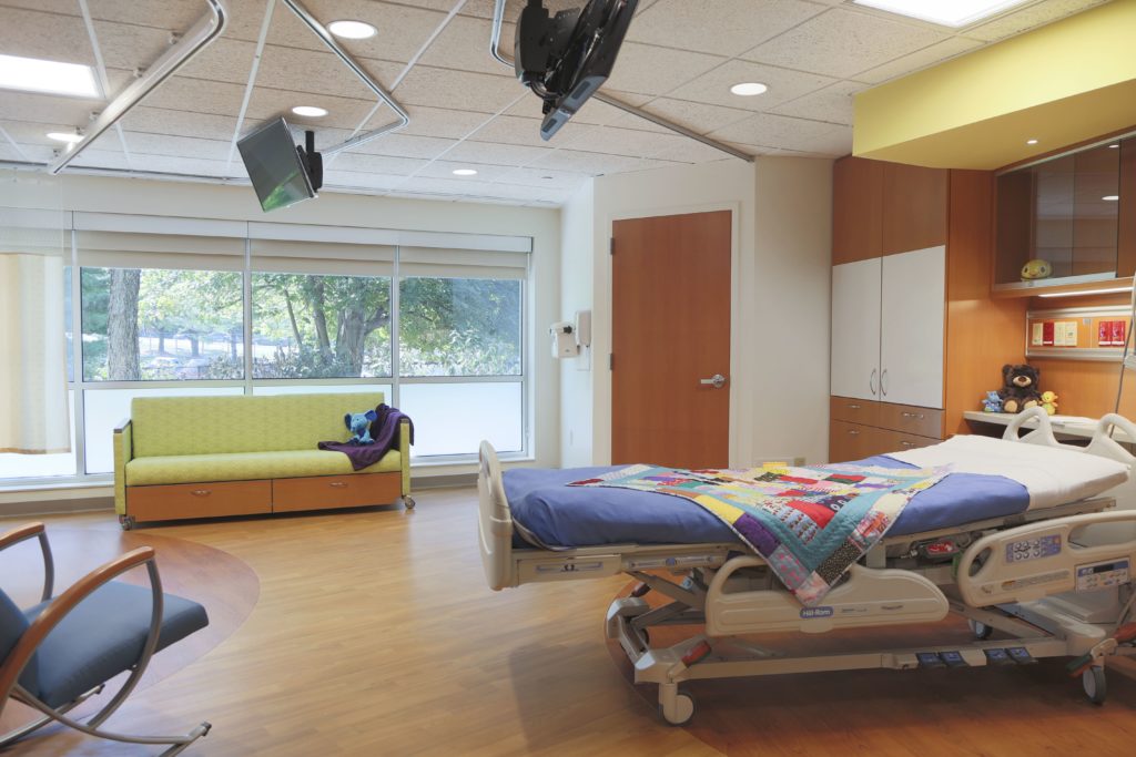 Hospital patient room with chair, couch and bed with colorful blanket