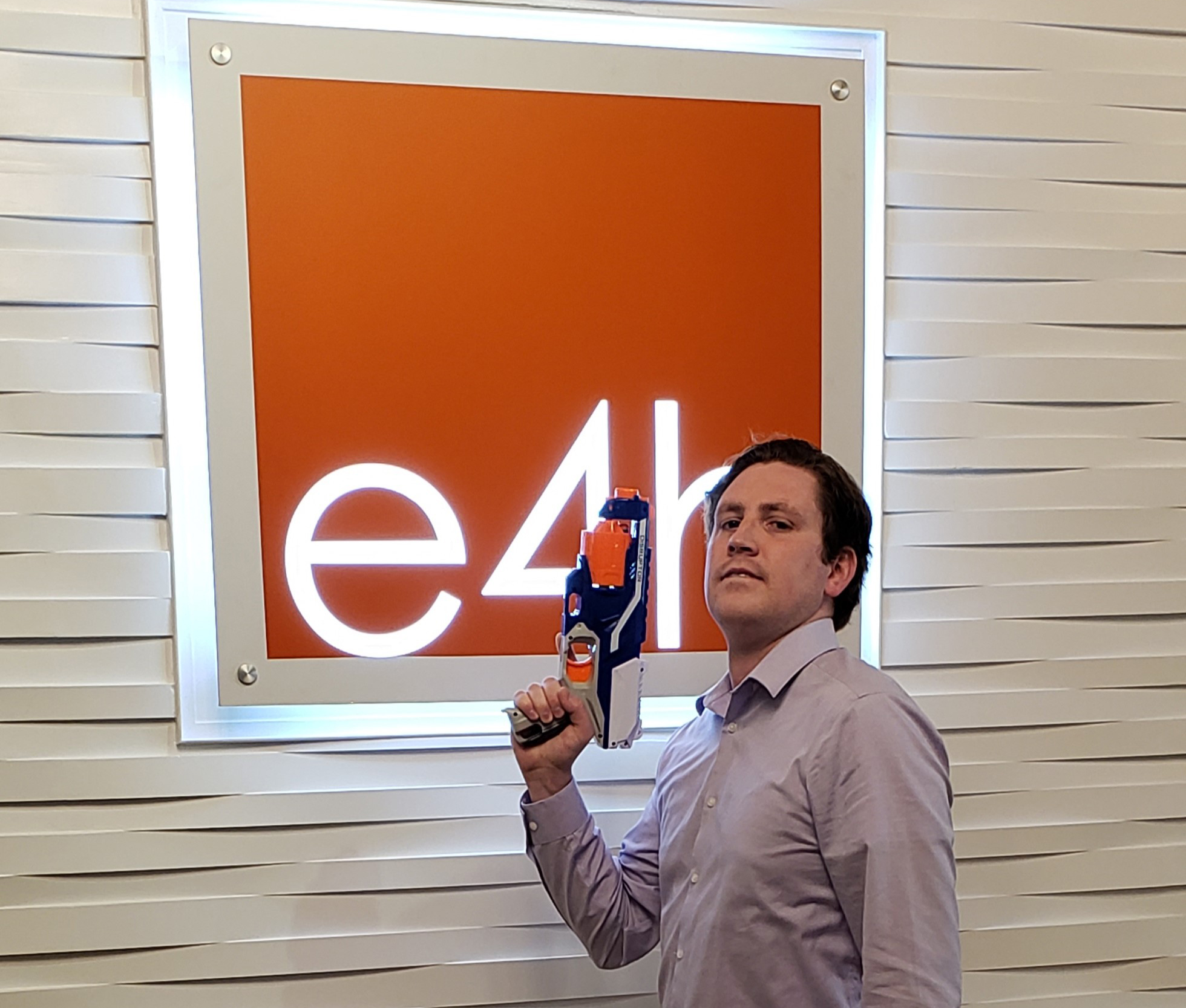 An intern poses with a Nerf gun in front of an E4H sign