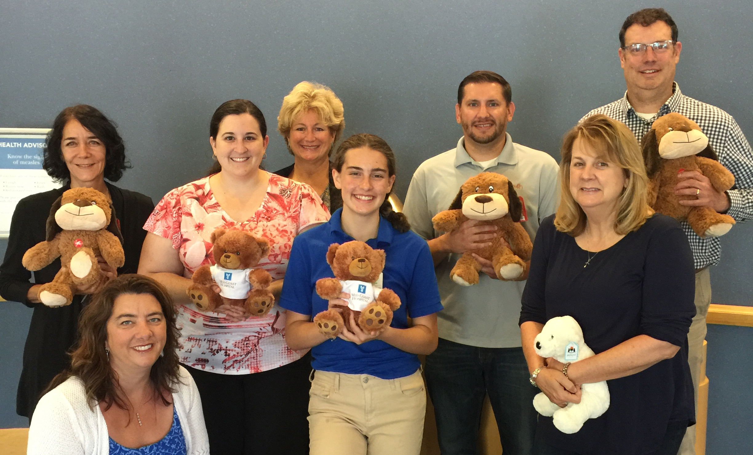 E4H Portland team members smile while holding up with teddy bears to donate to Mid Coast Hospital