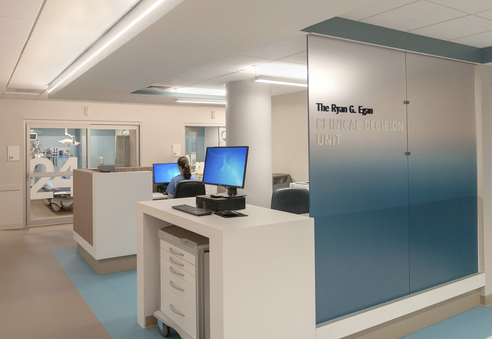Newport Hospital Emergency Department Clinical Decision Unit check-in area with computers, drawers and equipment, plus an exam room in the background