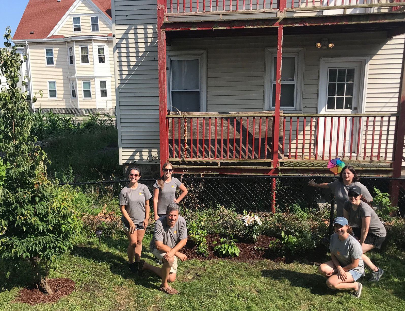 Group of six E4H team members smiling in front of the Bellevue Homeless Shelter's gardens