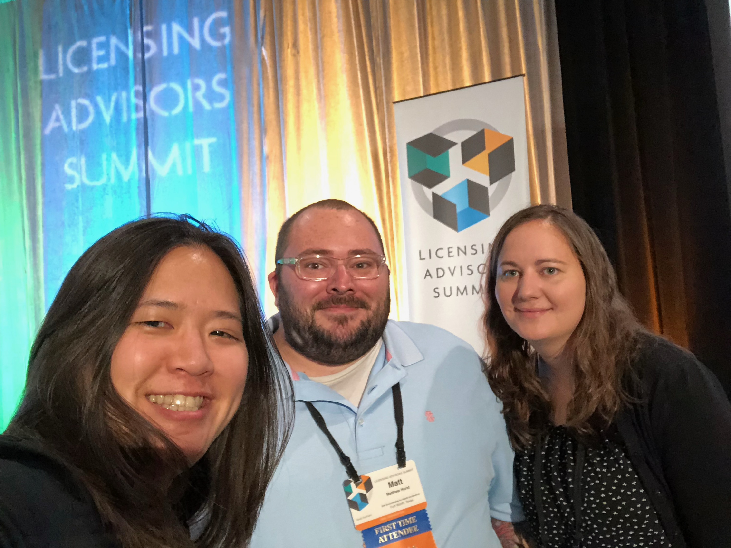 Three people smiling with stage curtain in background at the Licensing Advisors Summit in Minnesota.