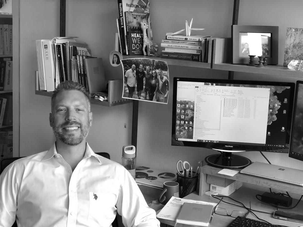 Man smiling at his desk next to a computer enjoying his work - Jason Lee in his office