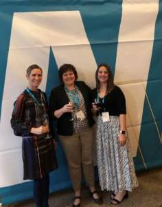 Three women E4H partners stand in front of blue and white AIA Women's Leadership Summit banner