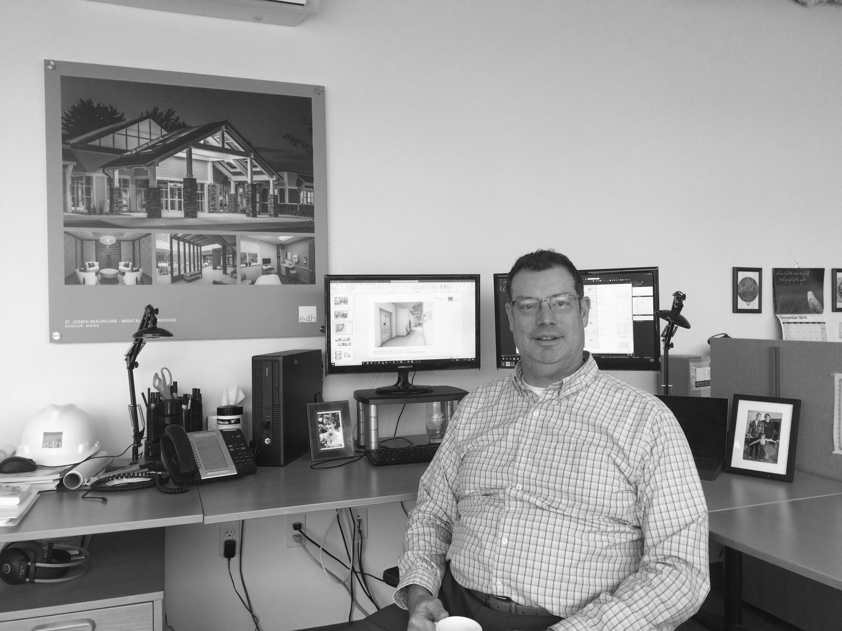 Jon Boyd, AIA Architect in his office with computer monitors and design photo on wall